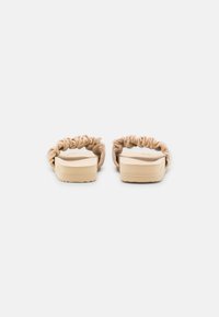 Beige slide sandals with gathered fabric upper and flat rubber sole; minimalistic design with a smooth texture.