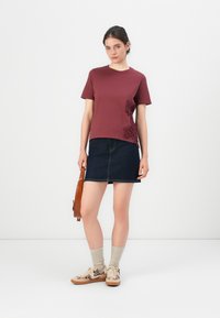 Burgunderfarget kortermet genser med blomsterbroderi på siden, i kombinasjon med en mørk denim miniskjørt og beige mønstrede sneakers.