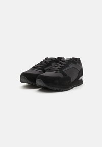 Zapatillas deportivas negras que combinan materiales de ante y textil, con una suela texturizada, cordones planos y un talón acolchado para mayor soporte.