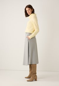 Light yellow turtleneck sweater with ribbed cuffs, paired with a knee-length, light gray A-line skirt and tan suede knee-high block-heel boots.