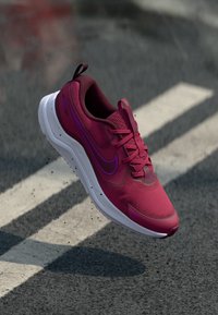Nike bėgimo bateliai ryškiai magentine spalva su tinkleliu viršuje, tekstūruotas paviršius, baltas pado vidurys ir purpuriniai akcentai. Mėgaujasi paminkštinta apykakle ir raišteliais.