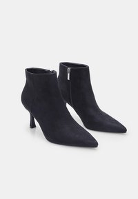 Bottines en suède noir avec un bout pointu et un talon haut et fin. Présentent une fermeture éclair sur le côté et une texture lisse.