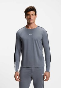 Graues Langarmshirt mit schwarzen Seitenstreifen, ausgestattet mit einem Rundhalsausschnitt und einem weißen "BOSS"-Logo auf der Brust. Weicher, elastischer Stoff.