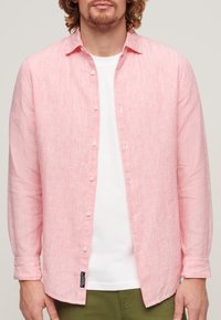 Camisa de manga larga a rayas rojas y blancas con cierres de botón, tejido suave y dobladillo redondeado, llevada sobre una camiseta blanca.