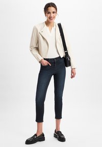 Crème leren motorjack, witte polo, donkere denim jeans en zwarte platform instappers. De outfit heeft een minimalistisch ontwerp en een slim fit.
