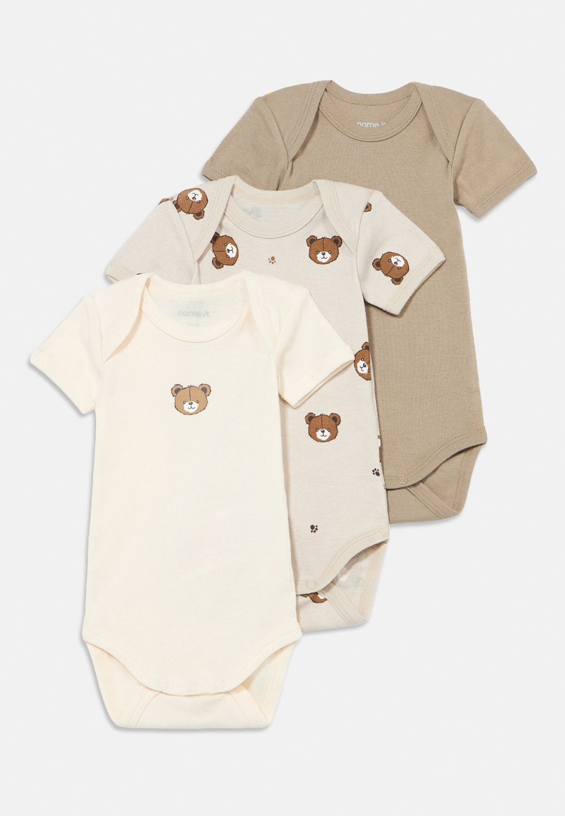 Tre kortermede babykroppsdeler i beige og krem. Den beige har et brunt bjørnemotiv, mens den kremfargede har et design av et bjørneansikt.