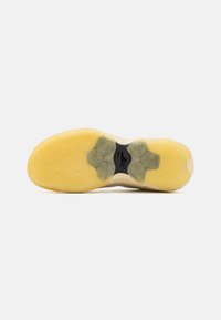 Sål af sko med struktureret gul gummi med cirkulære mønstre, en sort accent i midten og et let hævet kantdesign.