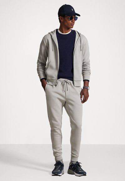 Svetlosivá mikina s kapucňou a tepláky, v kombinácii s námorníckym crew neck tričkom, námorníckou čiapkou a tmavými teniskami. Obsahuje šnúrku na stiahnutie v páse a bočné vrecká.