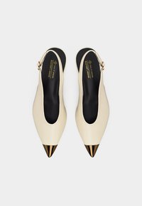 Μπεζ μπαλαρίνες με λουράκι πίσω, μυτερές χρυσές άκρες, μαύρες εσωτερικές σόλες και ρυθμιζόμενα λουράκια με χρυσή αγκράφα. Φέρουν την ένδειξη vegan και έχουν εκτυπωμένο το λογότυπο της μάρκας εσωτερικά.