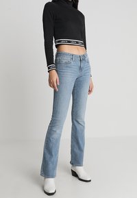 Svart korttröja med vitt "Levi's"-logotyp, tillsammans med ljusblå utsvängda jeans. Skorna är vita ankelstövlar med klossklack.