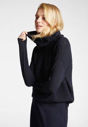 Top blu navy con design a costine testurizzato, colletto alto e maniche lunghe. Il tessuto appare morbido e leggermente elastico. Nessuna chiusura visibile.