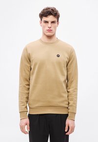 Béžová mikina s okrúhlym výstrihom, vyrobená z hladkej bavlny, s dlhými rukávmi a jemne vyšívaným logom na hrudi.