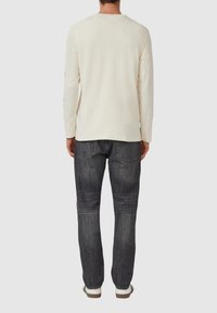 Crèmekleurig katoenen overhemd met lange mouwen. Achteraanzicht toont een ontspannen pasvorm. Gecombineerd met donkerblauwe denim jeans en witte sneakers.