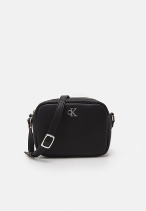 Czarna prostokątna skórzana torba na ramię z regulowanym paskiem i srebrnym logo Calvin Klein na środku z przodu.
