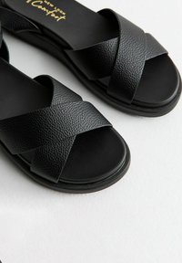 Sandalias negras con un acabado de cuero texturizado, que cuentan con un diseño de tiras entrecruzadas y una suela plana.