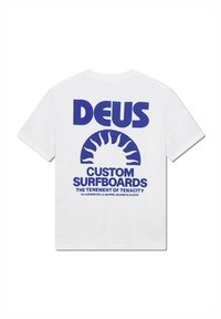 Camiseta de algodón blanca con un gran texto gráfico azul en la espalda: "DEUS CUSTOM SURFBOARDS" sobre un diseño de sol. Corte recto, mangas cortas.