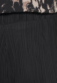 Tejido negro plisado con una superficie texturizada. Parcialmente cubierto por una blusa estampada, que muestra un sutil contraste de diseño.