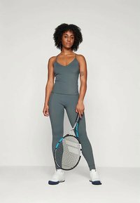 Atletska obleka v temno sivi barvi, ki vključuje oprijet zgornji del in legice. Dopolnjena z teniškim rekvizitom in belim obutvijo.