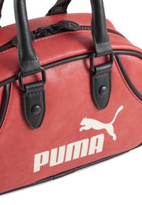 Crvena torba od umjetne kože s crnim akcentima, s dvostrukim ručkama i istaknutim bijelim Puma logom. Zatvaranje na munjevitu.