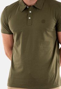 Polo olive en tissu doux, avec un col à boutons et un petit logo brodé sur la poitrine gauche. Manches courtes.