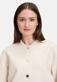 Jasnobeżowa bluza z okrągłym dekoltem, ściągaczami na mankietach i trzema złotymi guzikami z przodu. Miękka w dotyku, luźny krój, minimalistyczny design.