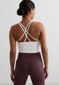 White sports bra with crisscross straps and a fitted design, paired with high-waisted, burgundy leggings in a smooth, stretchy fabric.