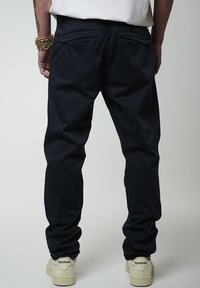 Chino blu navy con design a gamba dritta, tasche posteriori e una texture liscia, abbinati a sneaker Reebok color crema.