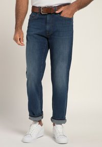 Jeans in denim con lavaggio scuro, fit dritto, con orli arrotolati. Abbinati a una cintura marrone e sneaker bianche. Texture liscia, stile classico.