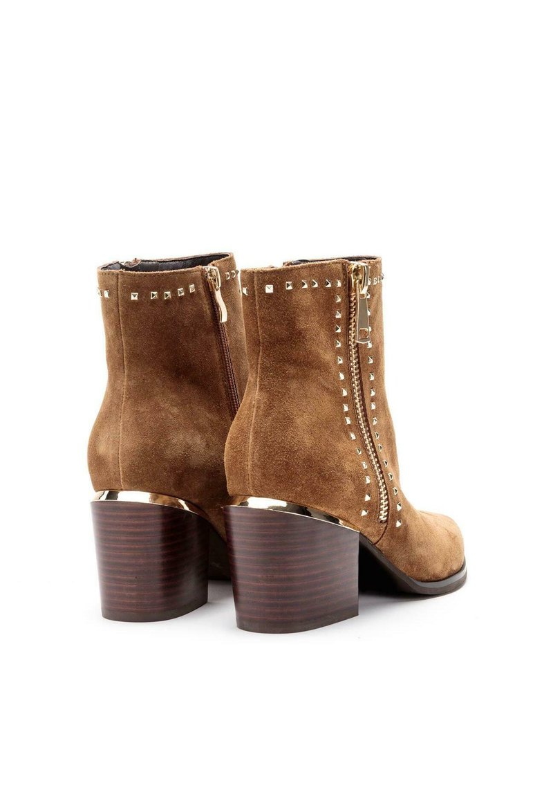 Braune Wildleder-Stiefeletten mit metallischen Nietenakzenten, seitlichem Reißverschluss und gestapeltem Holzabsatz. Glatte Textur mit passgenauer Form.