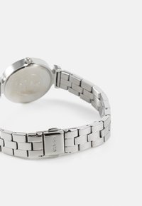 Montre en acier inoxydable argenté avec un cadran rond, un bracelet à maillons et une fermeture à clapet. Texture lisse avec une finition polie.