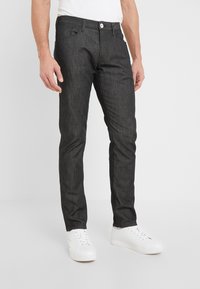 Tmavě šedé džíny s úzkým střihem, které mají klasický design s pěti kapsami a bílé zapínání na knoflík. V kombinaci s bílými teniskami.