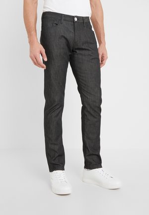 Donkergrijze denim broek met een slim fit, voorzien van een klassieke vijf-pocketontwerp en een witte knoopsluiting. Gepaard met witte sneakers.