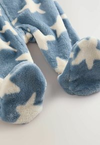 Ljusblå fleece pyjamas med fötter och vita stjärnm�önster. Mjuk textur, rundade fötter och dragkedjestängning. Lämplig för komfort och värme.