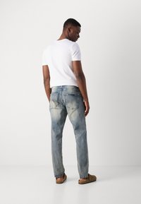 Light blue denim jeans with a faded finish, straight leg design, and back pockets. Worn with a plain white t-shirt and brown footwear.