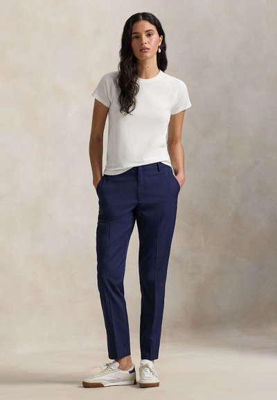 Balts kokvilnas T-krekls ar īsām piedurknēm, valkāts kopā ar tumši ziliem, speciāli pielāgotiem biksēm un baltām sporta kurpēm. Gluda tekstūra un piegulošs dizains.