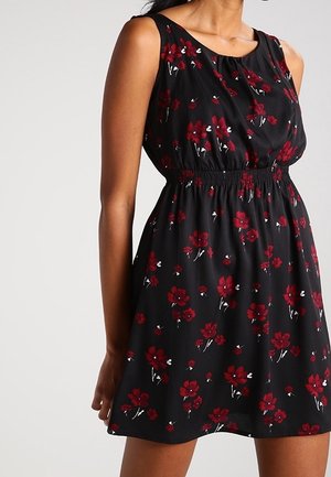 Sleeveless black dress with red floral pattern, gathered waist, and a relaxed fit on a standing person.