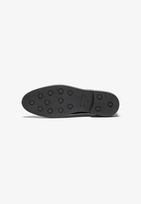 Semelle de chaussure noire en caoutchouc texturé, avec des motifs de prise circulaires et un bord lisse. Pas de branding ni de motifs visibles.