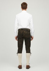 Bruna lädershorts med sidofickor, kombinerat med ljusa stickade strumpor. Modellen visad bakifrån, iförd en vit skjorta.