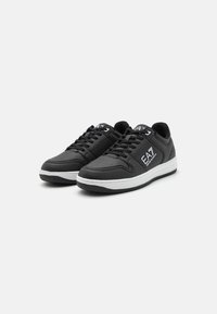 Sneaker nere realizzate in materiale sintetico liscio con punte perforate, suola bianca e logo EA7 sul lato. Chiusura con lacci.