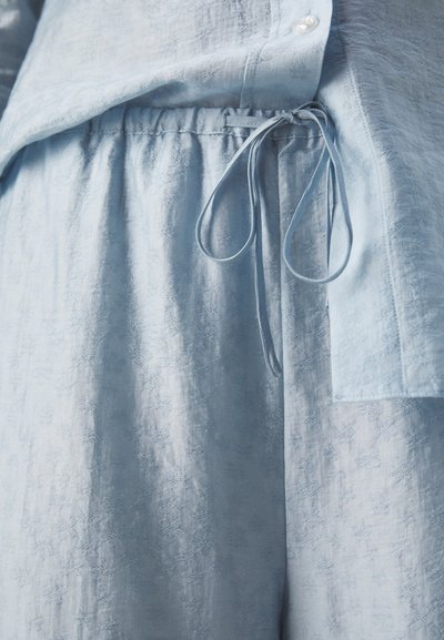 Ensemble comprenant un blouse et un pantalon bleu clair en tissu texturé, avec une taille à cordon de serrage et une fermeture à boutons, agrémenté de motifs floraux discrets.