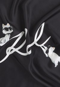 Deux chats blancs portant des lunettes de soleil noires interagissent avec de grands textes cursifs blancs sur un tissu noir aux plis doux.