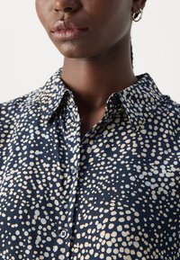 Navy patterned shirt featuring irregular light blue and cream dots, classic collar, button front, and soft fabric texture.