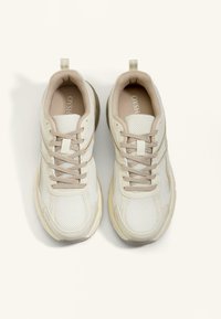 Leichte weiße Sneaker mit beigen Akzenten, Obermaterial aus Mesh, gepolsterter Sohle und flachen Schnürsenkeln. Mit Zuglasche an der Ferse.
