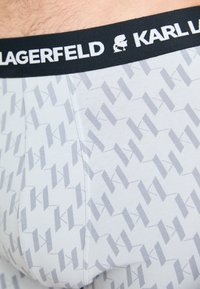 Sive uzorčene bokserske gaće s crnim pojasom u kojem je bele "Karl Lagerfeld" oznake i ponovljenim geometrijskim dizajnom.