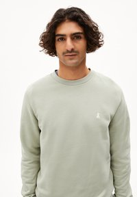 Hellgrüner Sweatshirt aus weichem Stoff, mit langen Ärmeln und rundem Hals. Kleines weißes Logo-Detail auf der Brust.