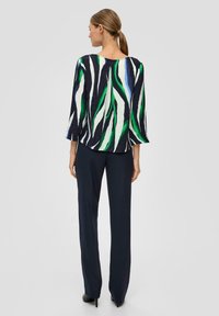 Texturierte Bluse mit einem auffälligen Muster aus grünen und marineblauen Streifen, kombiniert mit marineblauen Hosen und schwarzen Absatzschuhen. Eng anliegendes Design mit Dreiviertelärmeln.