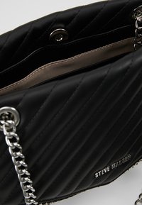 Borsa a tracolla in pelle nera trapuntata con una catena argentata, dotata di chiusura a scatto e fodera interna beige. Nome del marchio impresso sul lato.