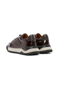 Sneakers in pelle marrone con accentuazioni testurizzate, una suola nera robusta e una intersuola bianca a contrasto. Design arrotondato con un leggero tacco.