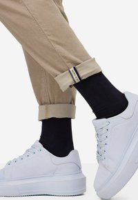 Pantaloni arrotolati beige chiaro con risvolto, calzini blu navy e sneaker in tela bianca con suola testurizzata e punta rotonda.