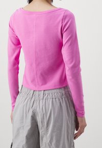 Långärmad topp i stark rosa bomull, med rund halsringning och rak skärning i fållen. Matchad med grå shorts med elastisk midja.